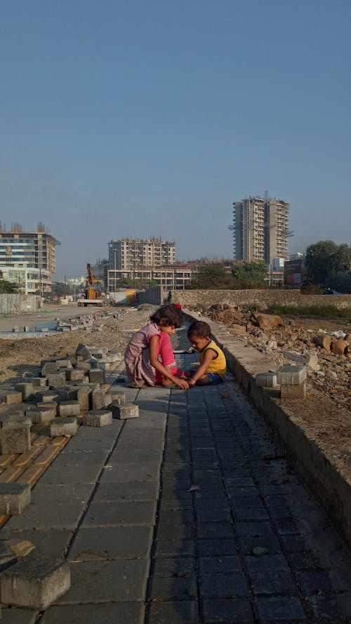 A Girl and a Boy Sitting on Pavers