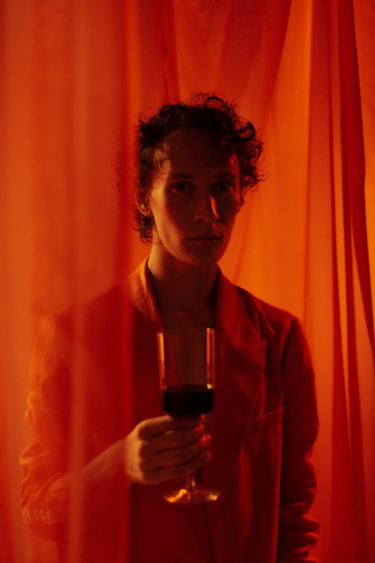 Man With Glass Of Wine Among Red Curtains