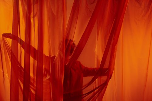 Free A silhouette of a dancer performing gracefully behind vibrant red curtains in a studio setting. Stock Photo