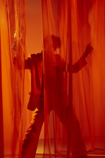 Artistic silhouette of a performer behind a dramatic red curtain in a studio setting.