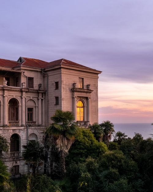 Free A beautiful historic mansion surrounded by palm trees on the coast of Sochi, Russia, captured at sunset. Stock Photo