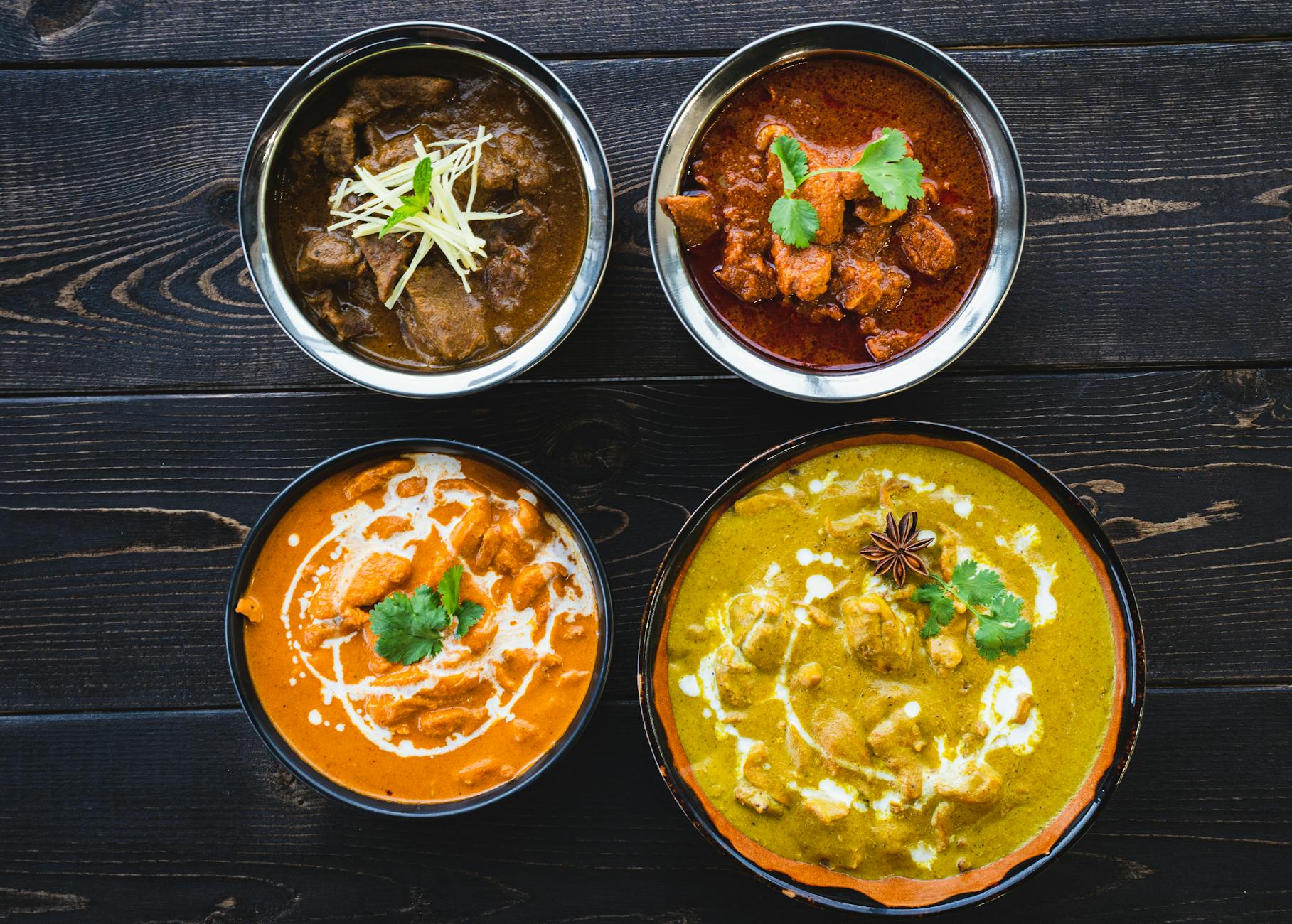 A spread of Indian curries with naan and rice on a rustic dark table.