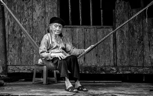 Grayscale Photo of an Elderly Woman Sitting on a Hammock