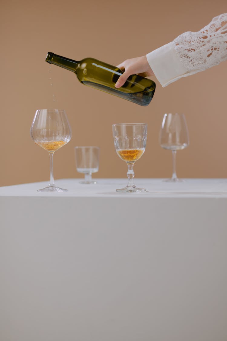 Hand Holding Wine Bottle Over Glasses On White Table