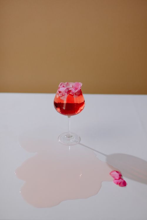 Free Aesthetic red cocktail with rose petals in a glass on a white table, elegantly spilled. Stock Photo