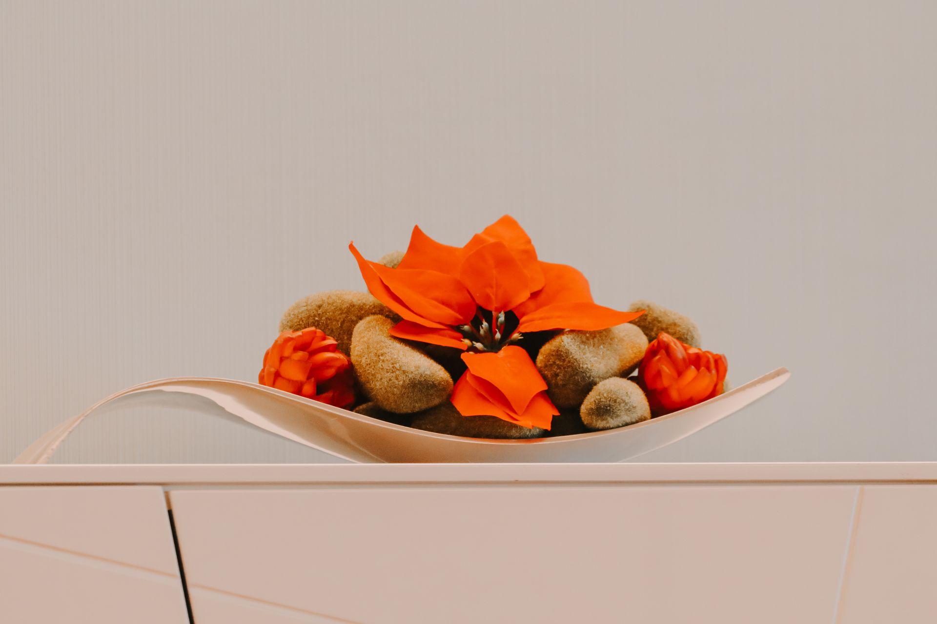 Modern decorative floral arrangement featuring vibrant orange petals and natural stones in a minimalist setting.
