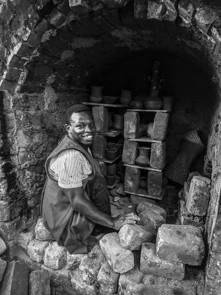 Black And White Photograph Of A Man Sitting In Pottery Oven