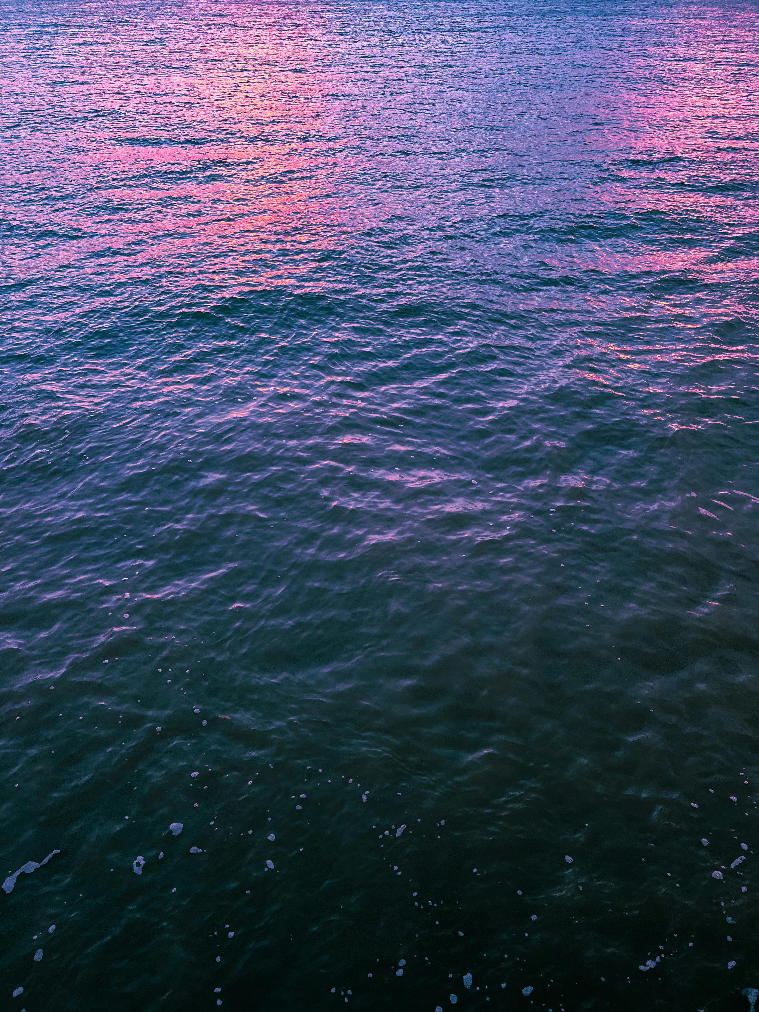 平静的海面，水中反射出充满活力的粉红色和紫色色调