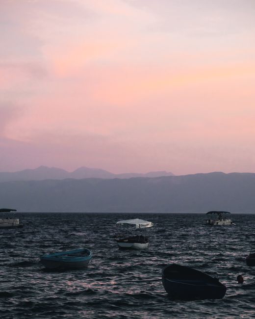 Calm sea at dusk with boats gently floating, hills in the distance.