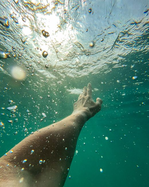 A captivating underwater shot of a hand reaching towards the surface, with sunlight filtering through the water.