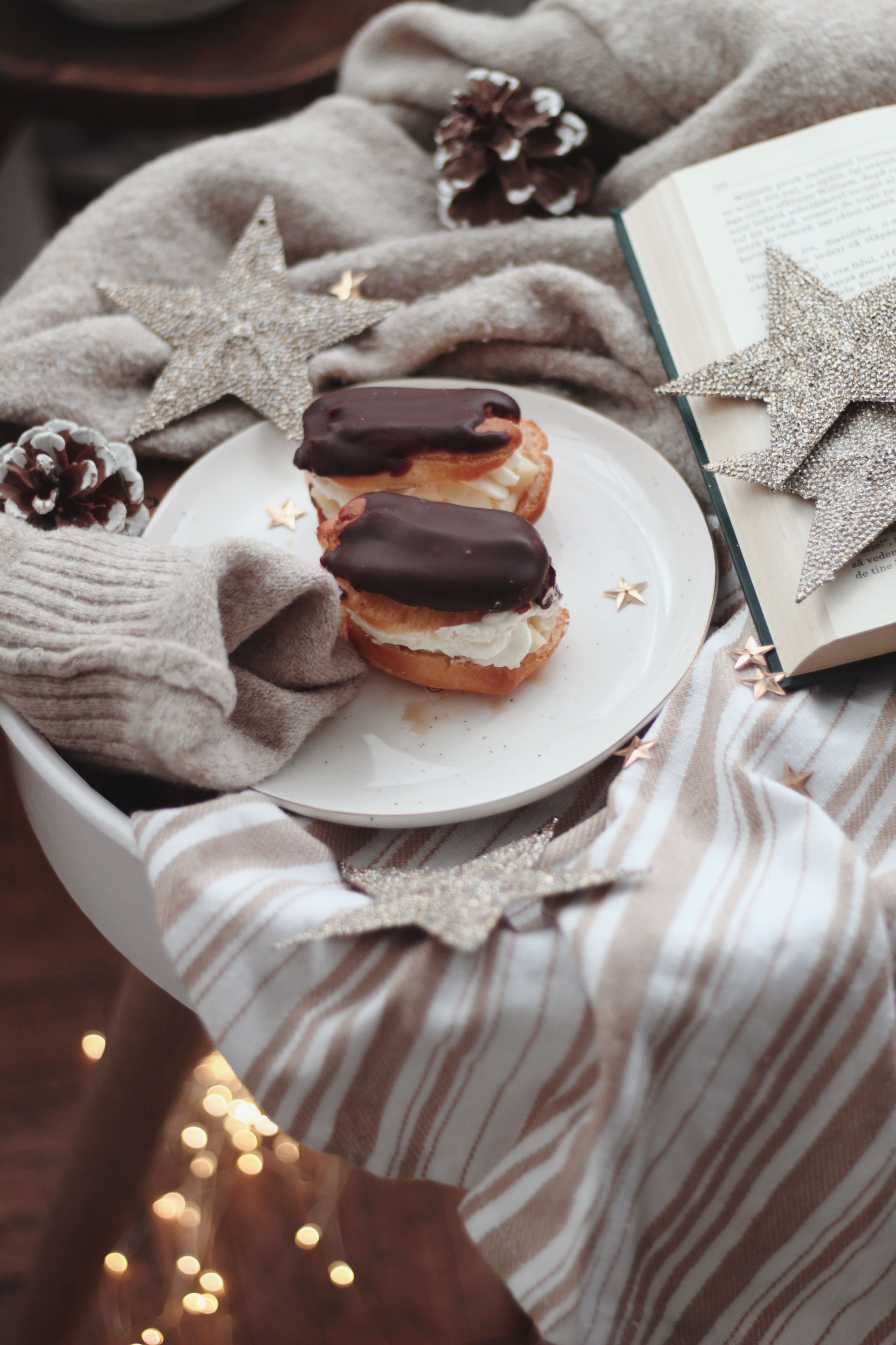 Warm winter setting with chocolate eclairs, a book, and festive decorations.