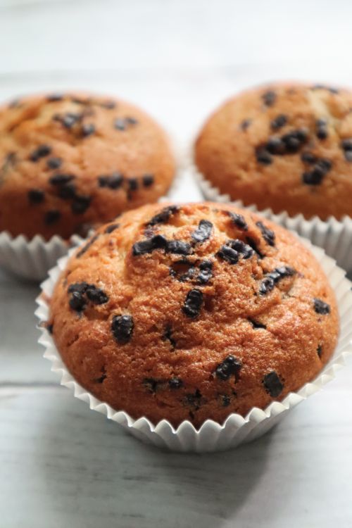 Free Close-up of freshly baked chocolate chip muffins in paper cups on a light wooden surface. Stock Photo