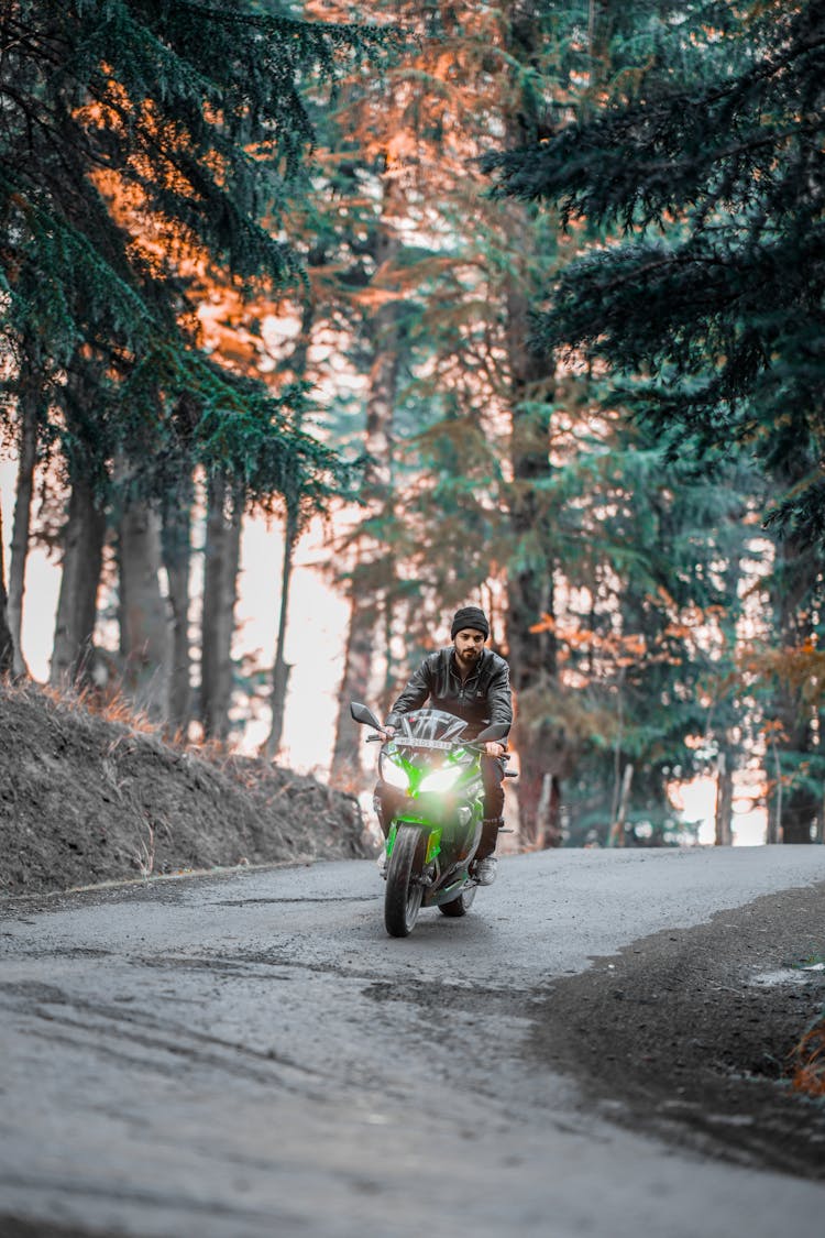 A Man Riding A Green Motorcycle On The Road