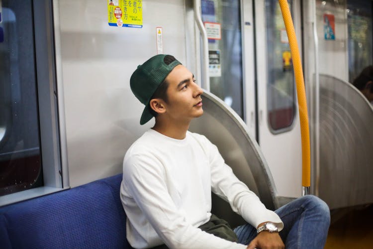 A Man In White Sweater Looking Up While Sitting Inside The Train