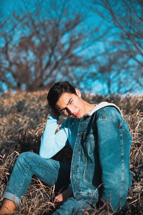 Free A Man in Denim Jacket and Jeans Sitting on Brown Grass Stock Photo