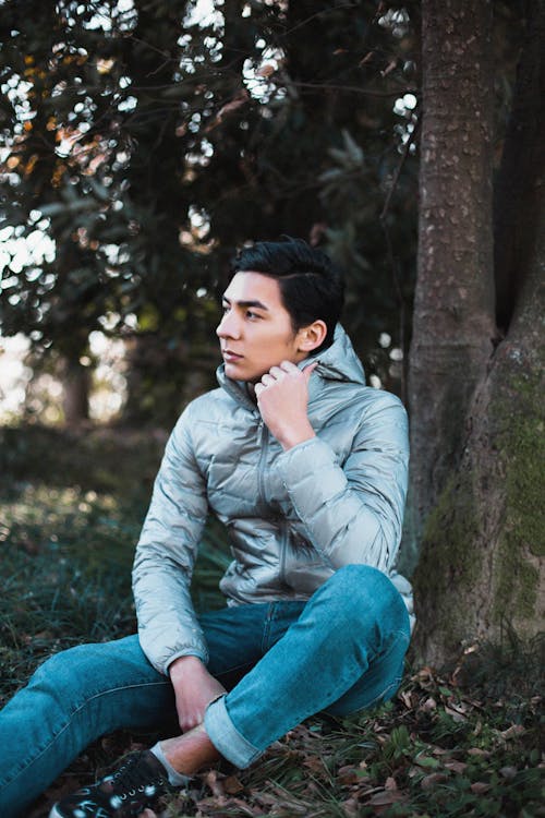 A Man in Denim Jeans Sitting on the Ground Near the Tree Trunk