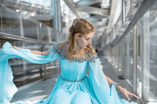 Elegant woman in blue gown seated in a contemporary indoor space.