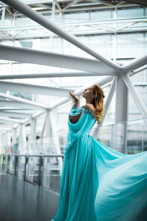 A Woman in Blue Long Gown Standing Near Glass Railing while Looking Up