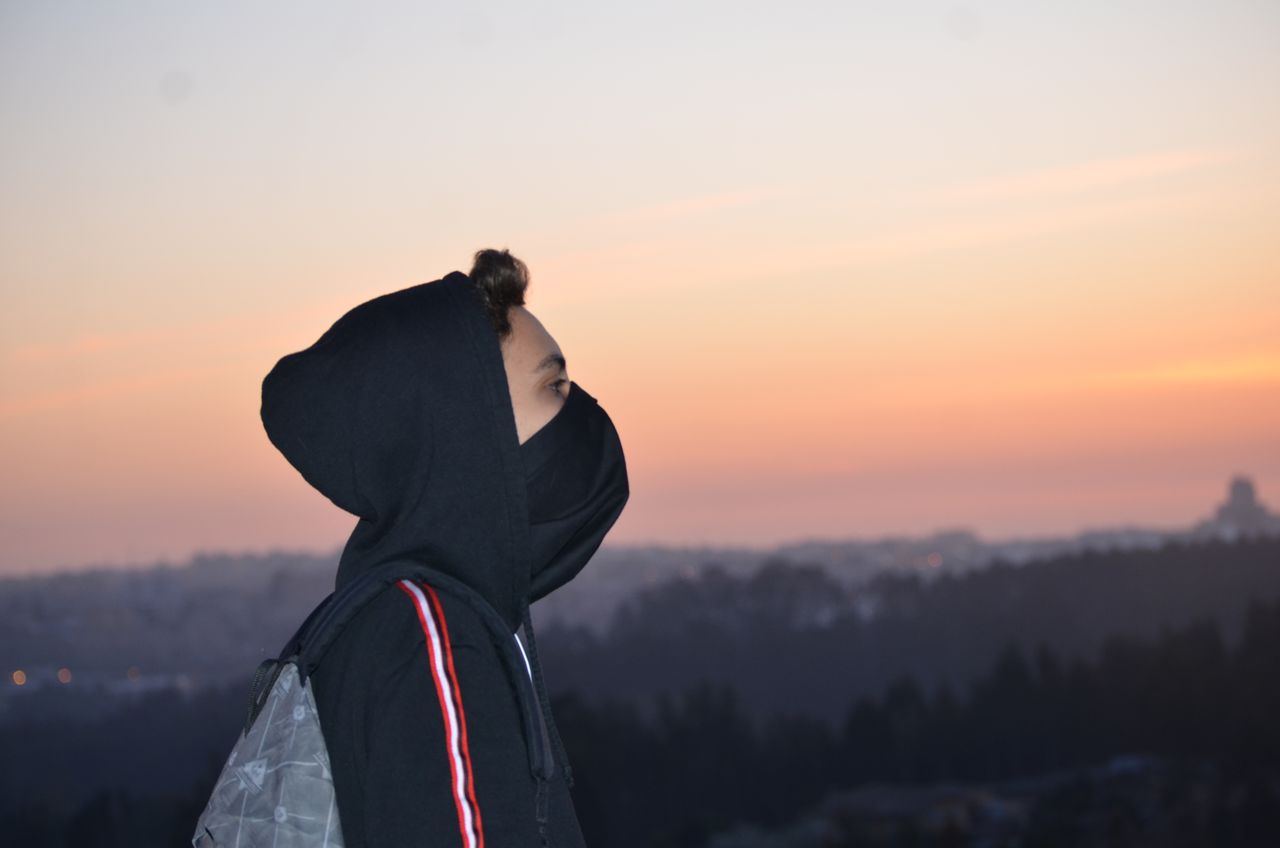 a person in a hoodie observing a picturesque sunset over a mountainous