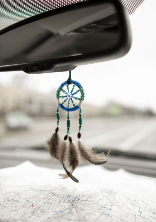 Free Part of car interior with little dreamcatcher hung as rearview mirror pendant above unfolded map Stock Photo