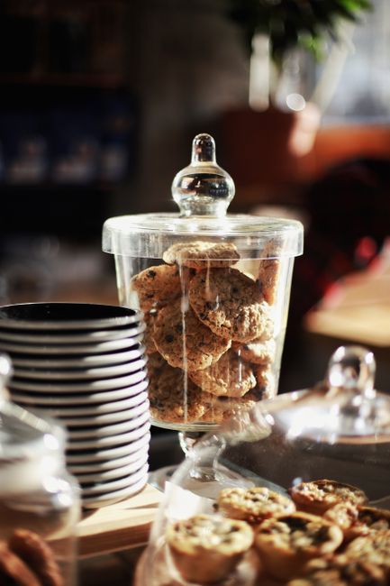 A glass jar of soft, clumped light brown sugar with a wooden spoon resting in it, next to a bottle of molasses.
