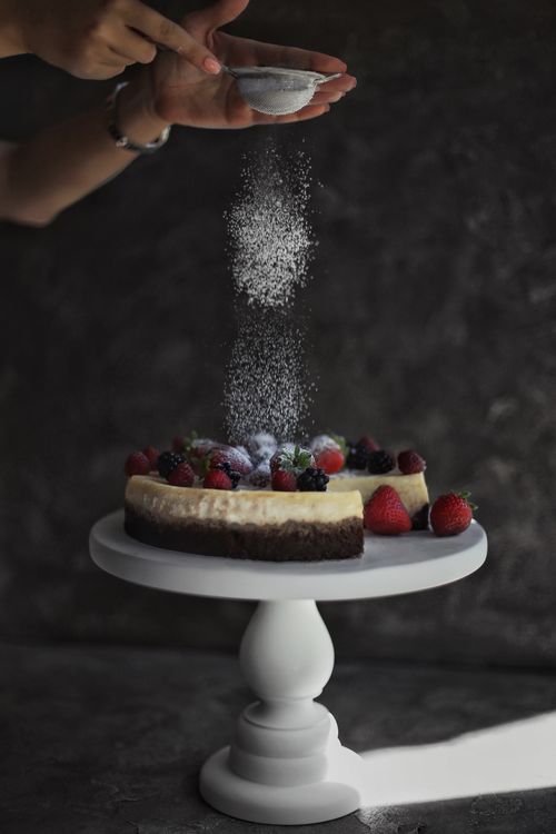 Free Elegant cheesecake with fresh berries being sprinkled with sugar, highlighting baking artistry. Stock Photo