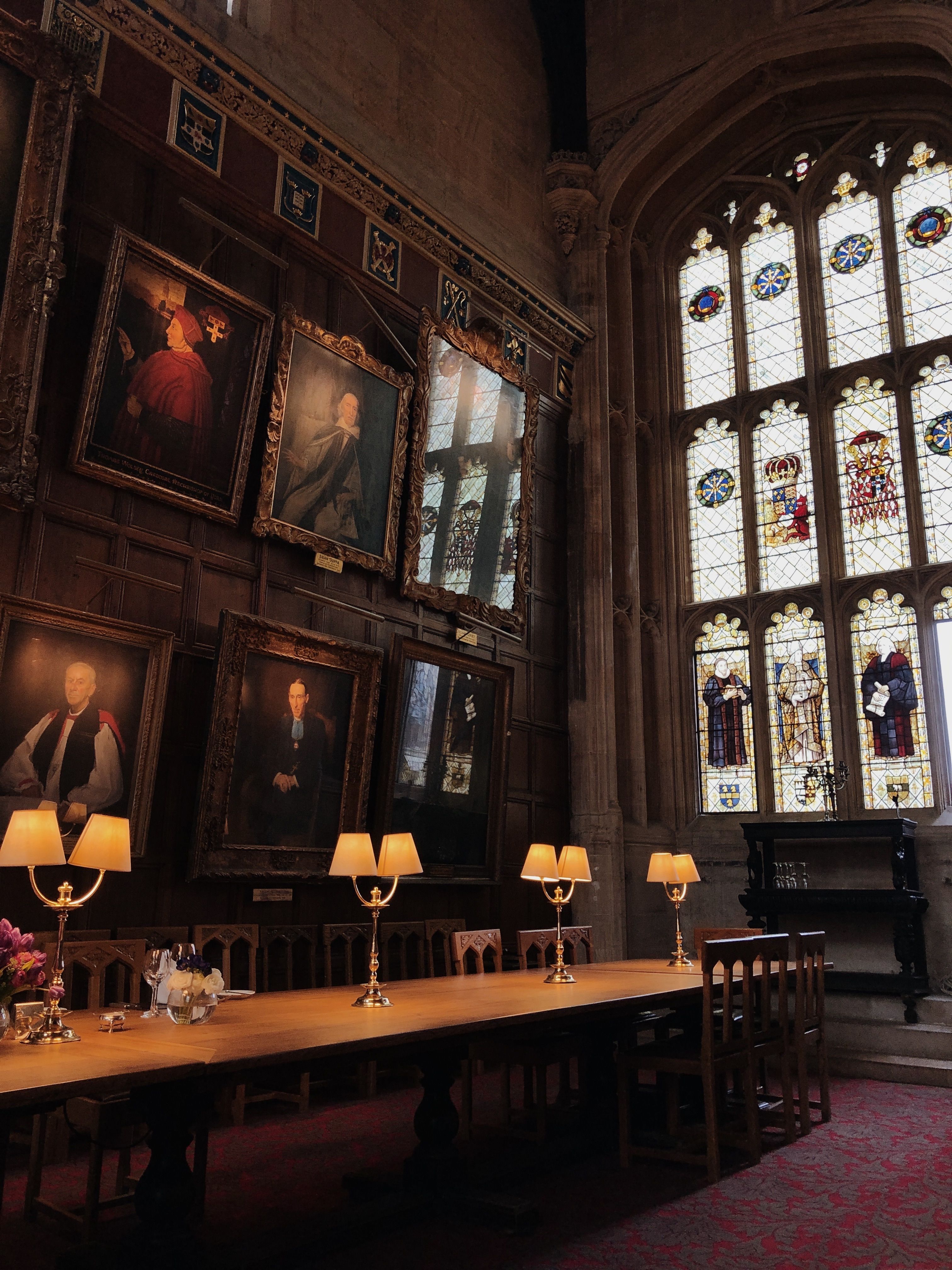 A beautifully decorated historic interior with stained glass windows and portraits in Oxford, England.