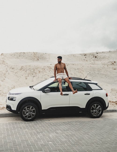 A Shirtless Man Sitting on Top of the Car