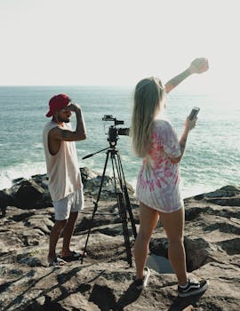 Two photographers with a tripod on a rocky shore capturing stunning ocean views.