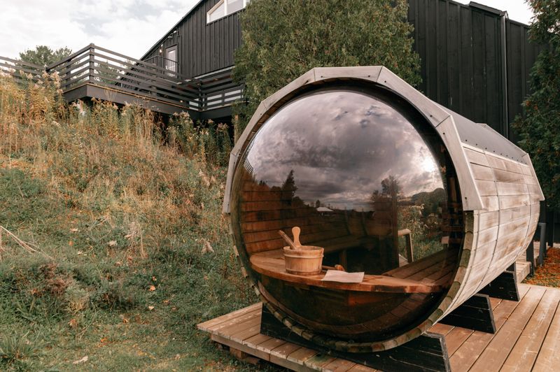 Rustic outdoor barrel sauna with glass front door set in a natural landscape