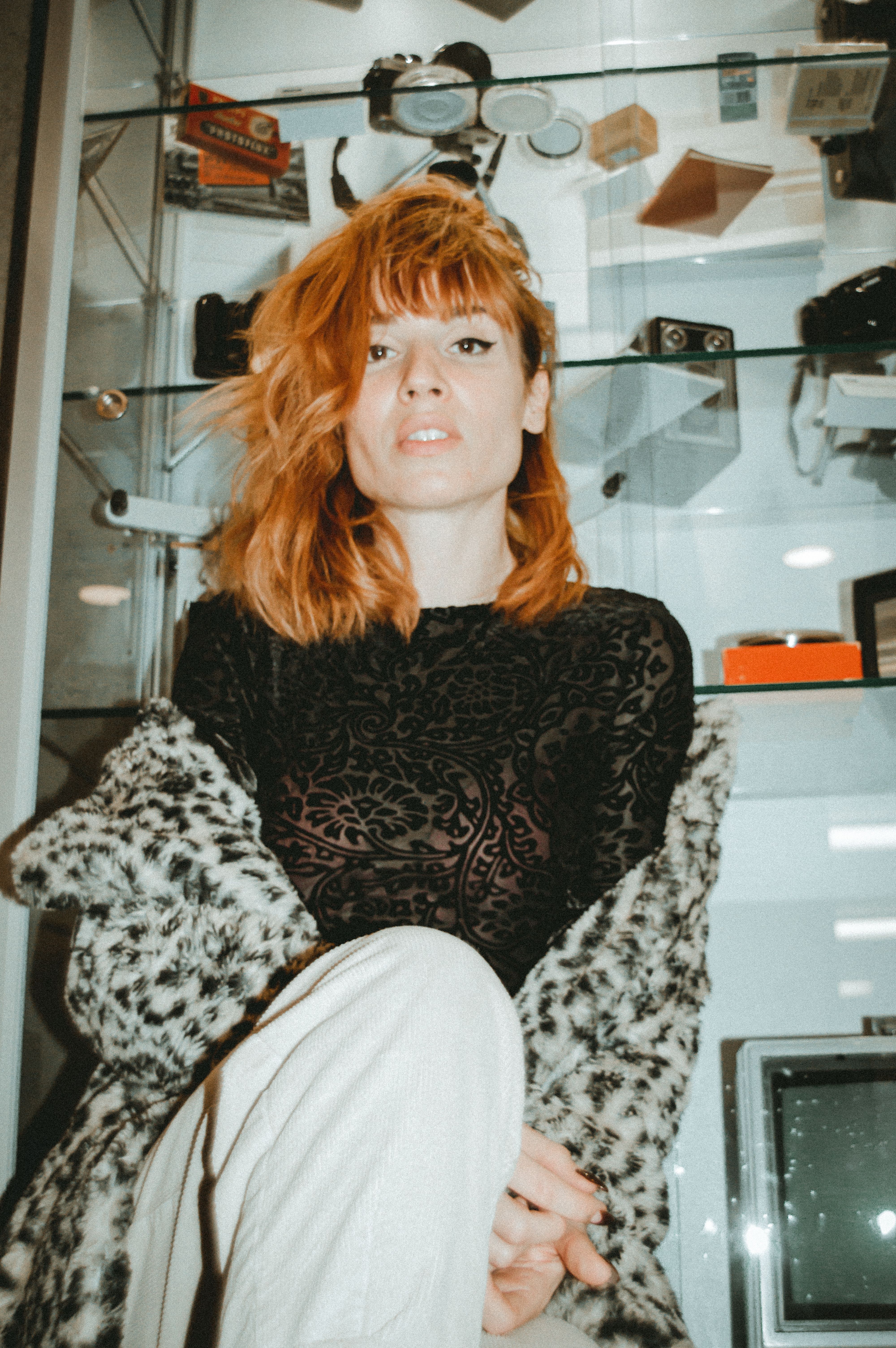 Stylish woman in leopard print and ginger hair posing in front of a retro display shelf.