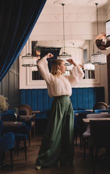 A fashionably dressed woman poses gracefully in a chic restaurant with stylish décor.