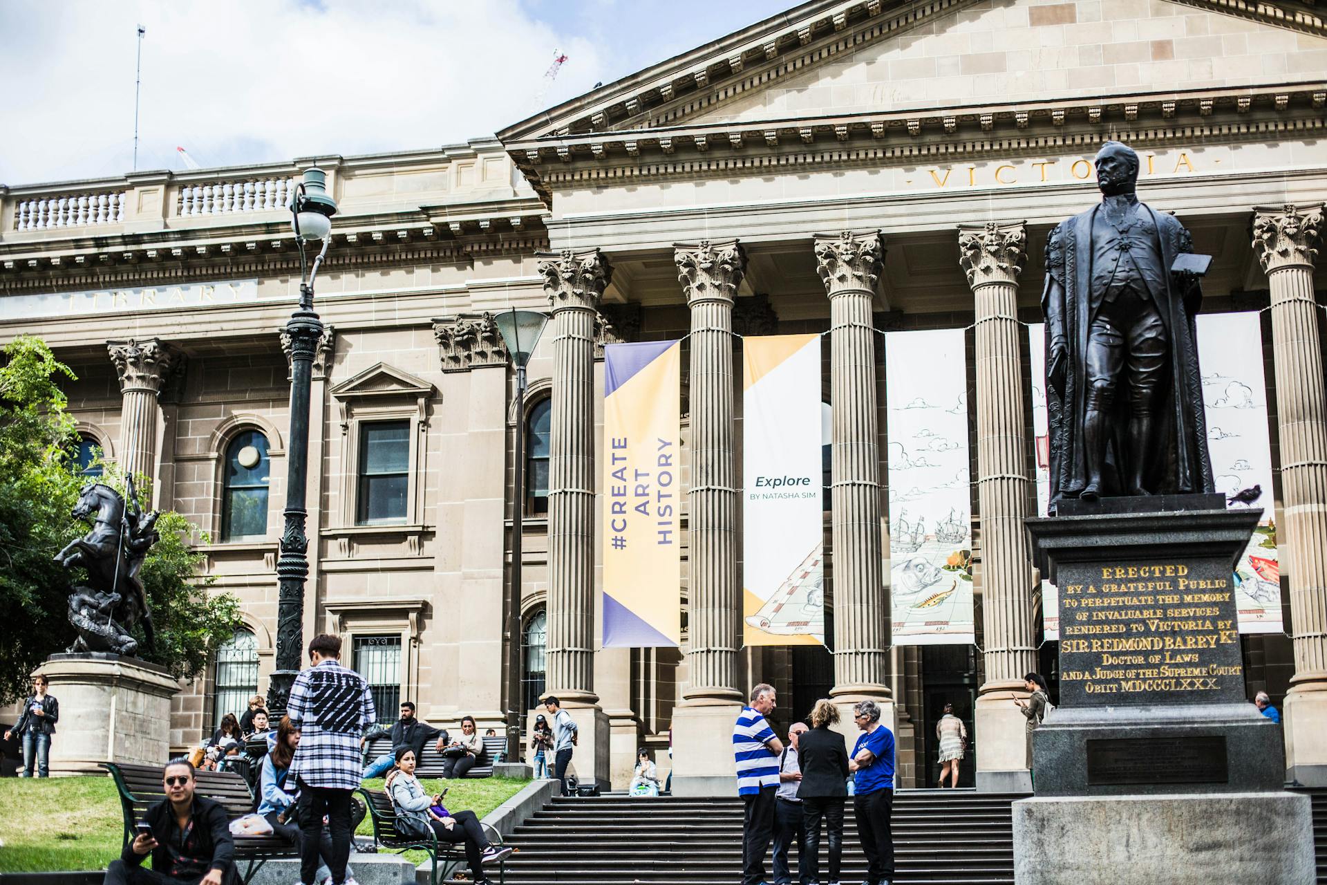 View of the State Library of Victoria with Sir Redmond Barry statue and visitors in Melbourne.