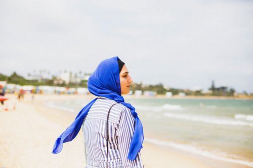 Free A woman in a blue hijab enjoys the serene view of an Australian beach, embodying tranquility and leisure. Stock Photo