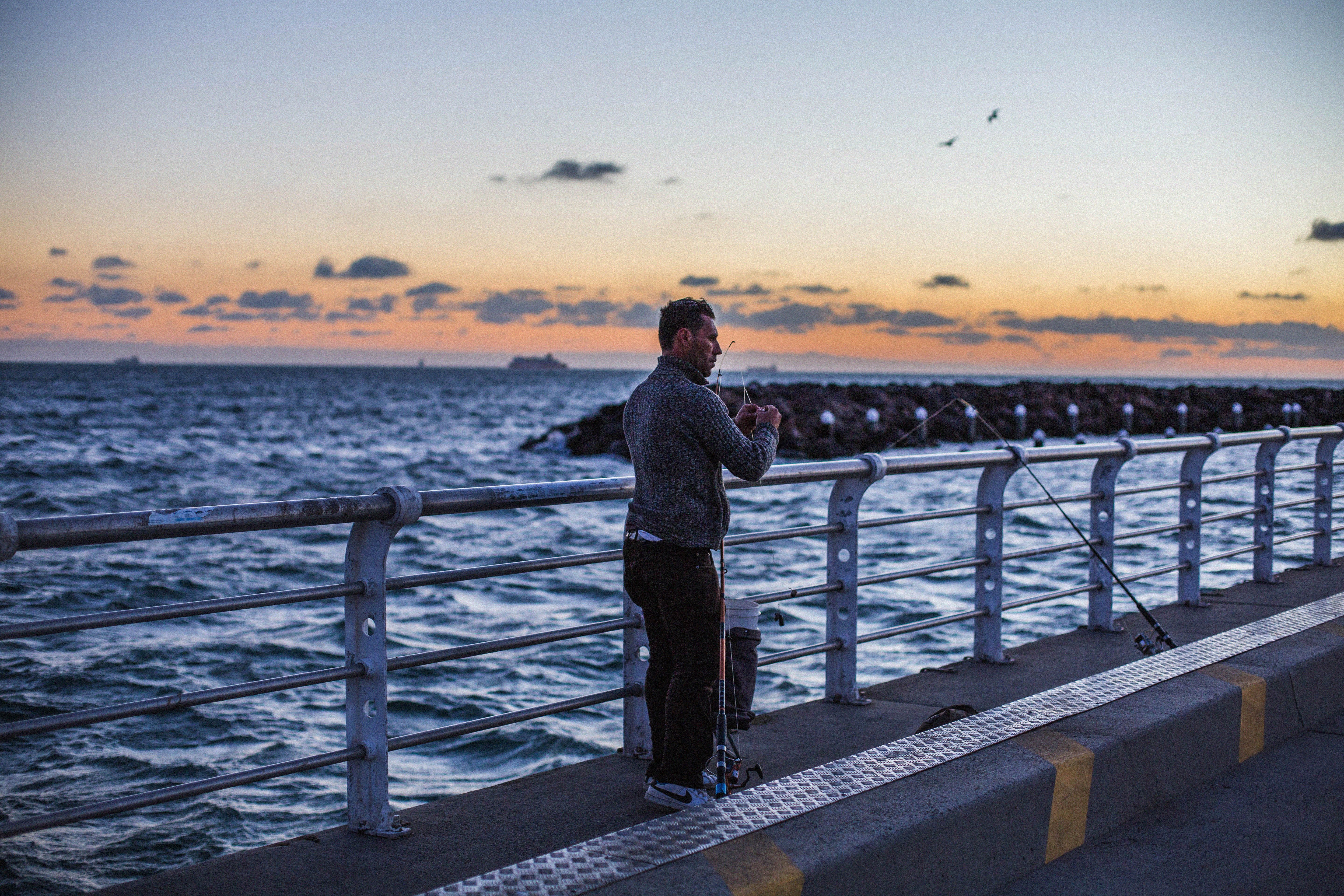 A man fishing on St Kilda Pier during a beautiful sunset with a view of the sea and sky.