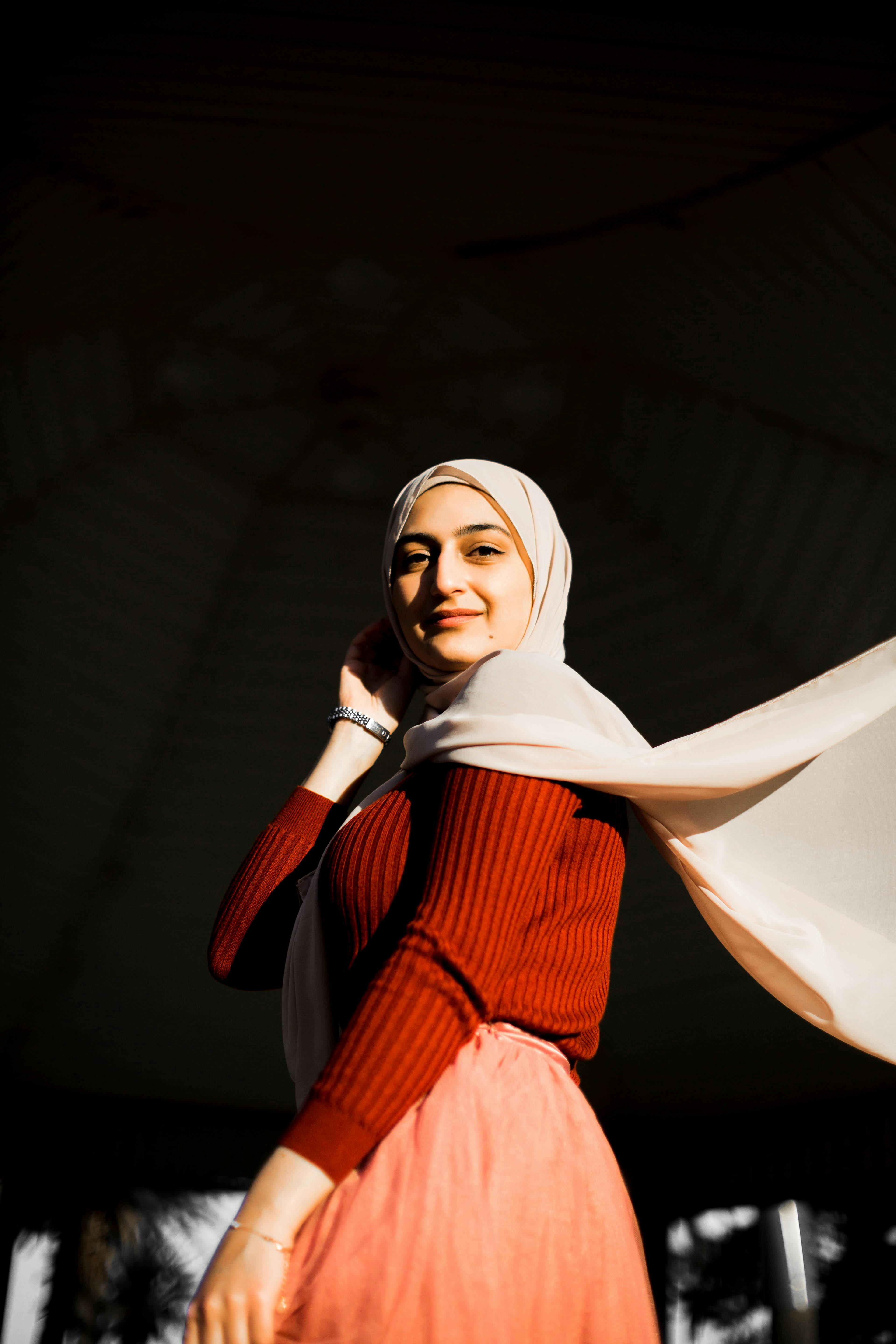 Portrait of a smiling woman in a headscarf, lit by sunlight in an outdoor setting, showcasing vibrant colors and warm tones.
