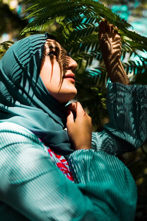 A Woman in Hijab Under Leaves of a Plant