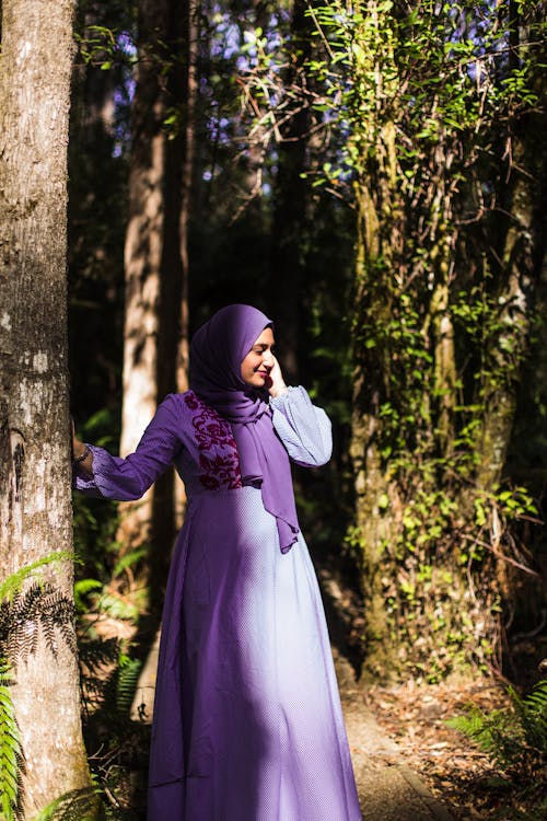 A Woman in Purple Dress Standing Beside Tree