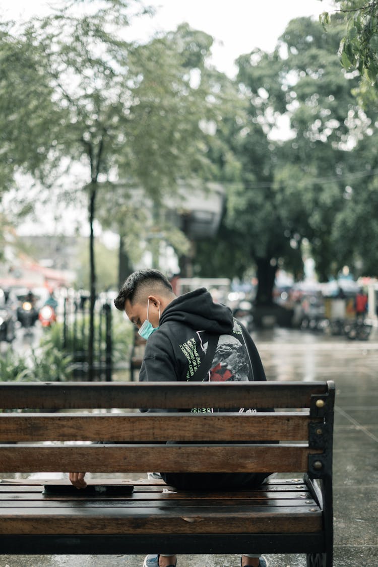 Young Man In A Face Mask Sitting On The Park Bench 