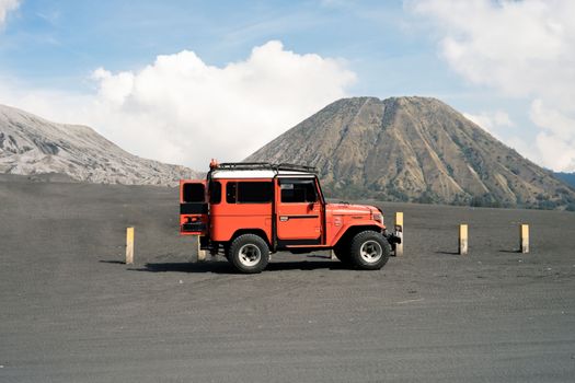 Red Jeep parked in Mount Bromo landscape, showcasing volcanic terrain in East Java, Indonesia.