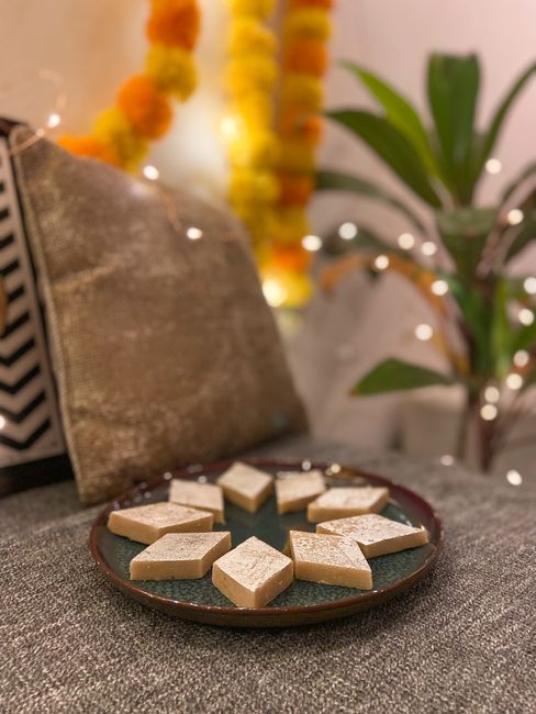 Diamond-shaped kaju katli pieces stacked on a plate, showing their pale ivory color and thin silver vark coating on top.