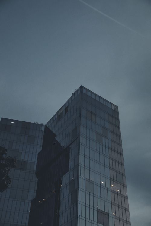 Free A modern skyscraper with glass facade standing tall against the muted evening sky. Stock Photo