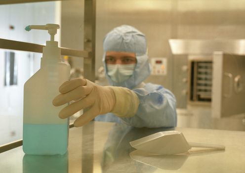 A scientist in protective gear reaching for a sanitizer bottle in a laboratory setting.