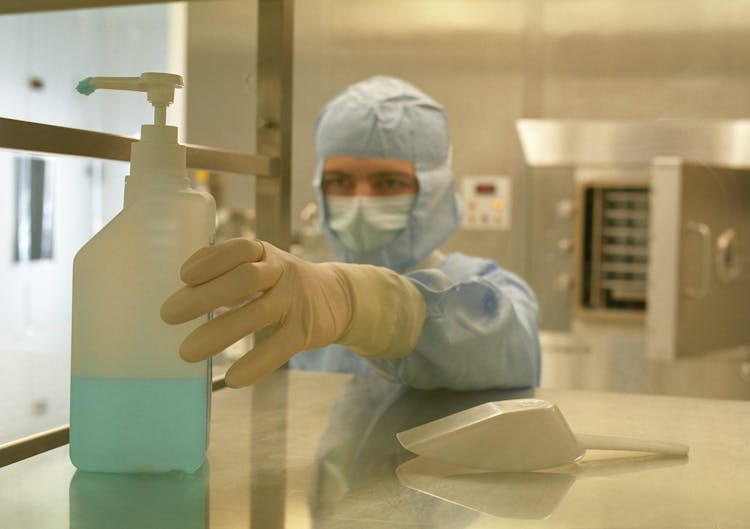 Man In A Disposable Medical Uniform Reaching Out A Container With Liquid