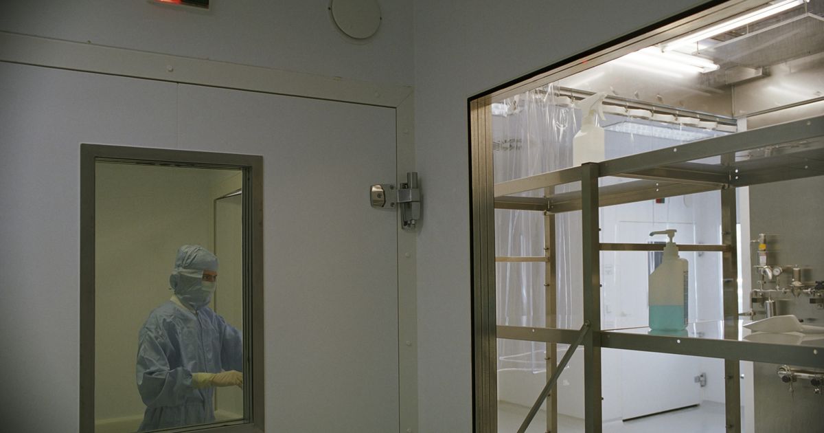 Reinraum mit Schleuse und Mitarbeiterin in Schutzkleidung als Einsatzort der Reinraumreinigung nach GMP