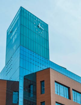 晴朗的天空下，现代摩天大楼的玻璃立面上设有一个突出的时钟，呈现低角度视图