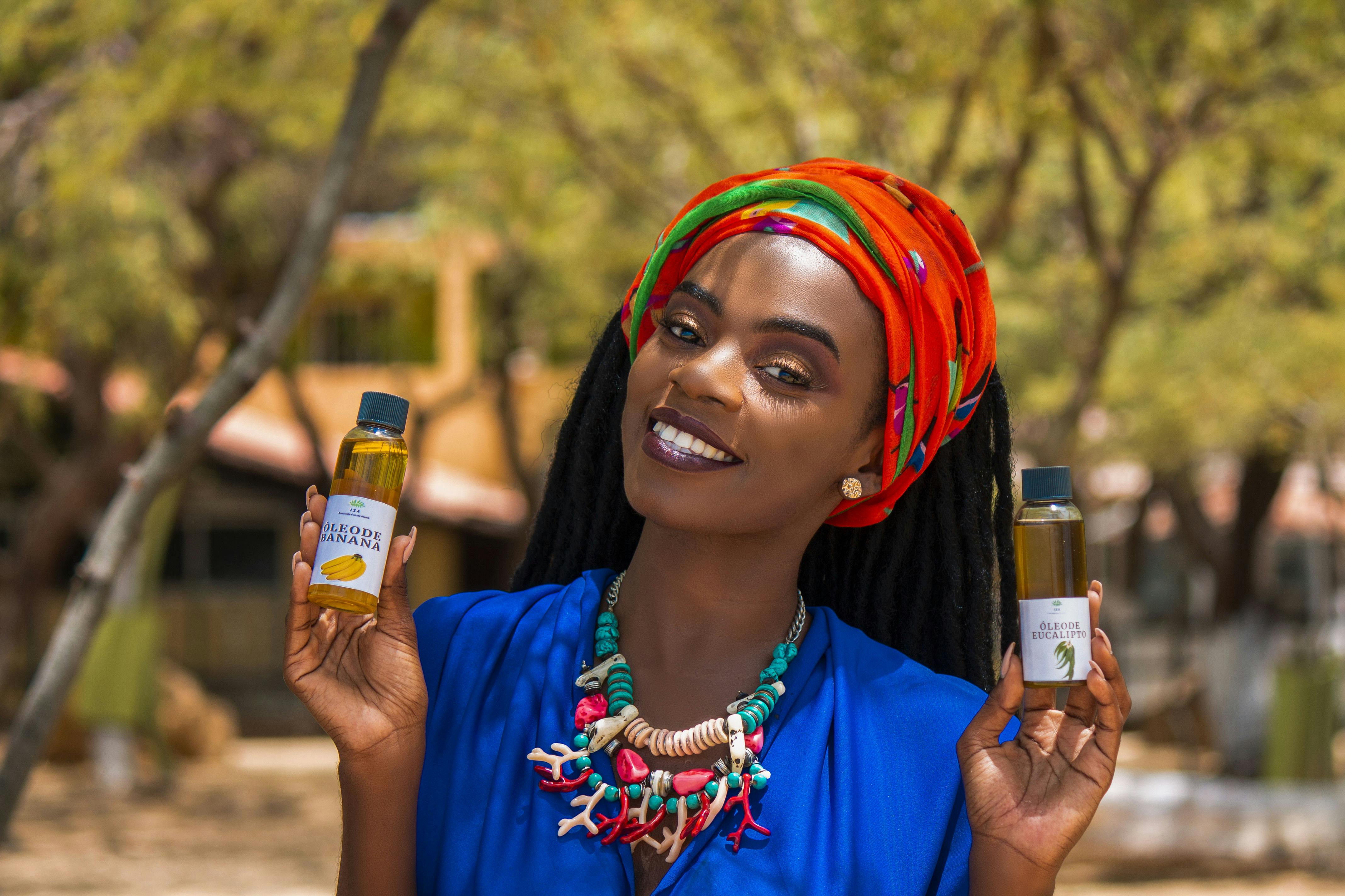 A beautiful African woman smiling while holding essential oil bottles in an outdoor setting.