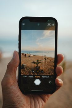 Close-up of hand holding a smartphone capturing a beach scene.