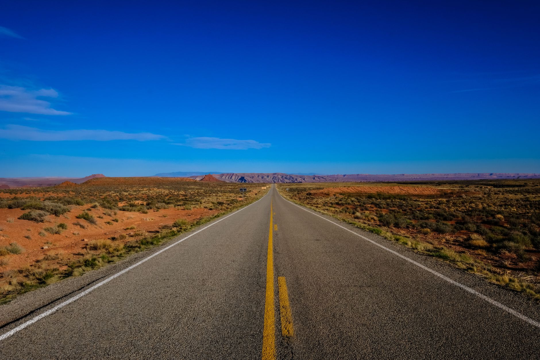 A straight highway stretches into the horizon through a desert landscape under a bright blue sky. Perfect for travel and adventure themes.