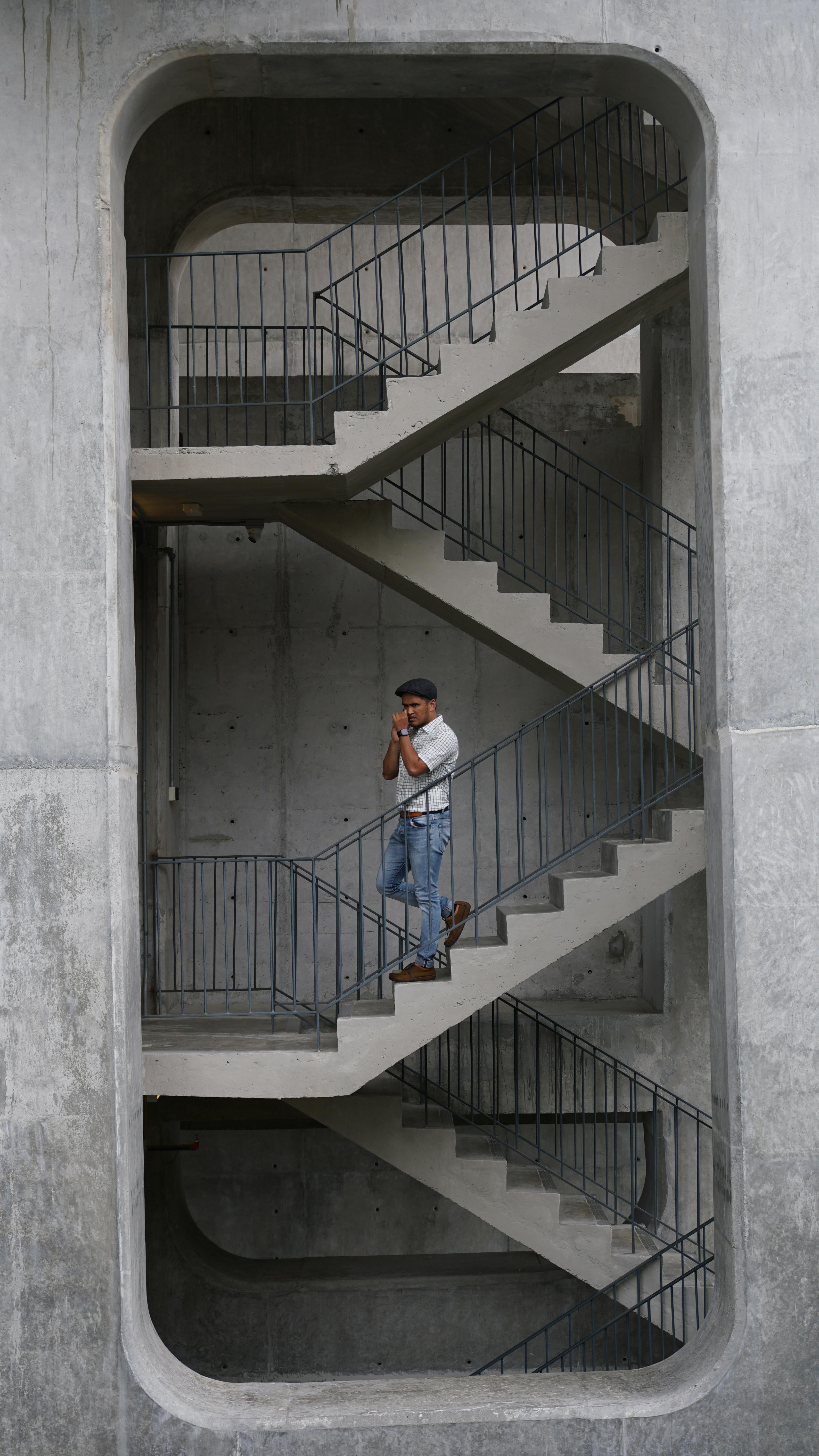 Person walking down a geometric industrial concrete staircase with metal railings.